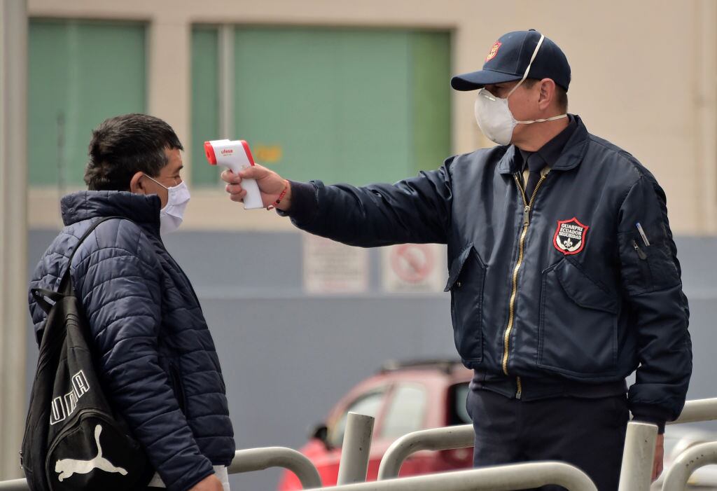Guardia toma la temperatura de pasajero en terminal de Quito