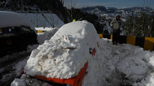 A man stands next to snow-covered card stucked on a road after a blizzard that started on January 7 and led to visitors being trapped in vehicles along the roads to the resort hill town of Murree, some 70 Kms northeast of Islamabad on January 9, 2022. - Army rescuers on January 9 cleared routes around the Pakistan hill town of Murree sheltering thousands of tourists after 22 people died in vehicles trapped by heavy snow. (Photo by Aamir QURESHI / AFP) (Photo by AAMIR QURESHI/AFP via Getty Images)