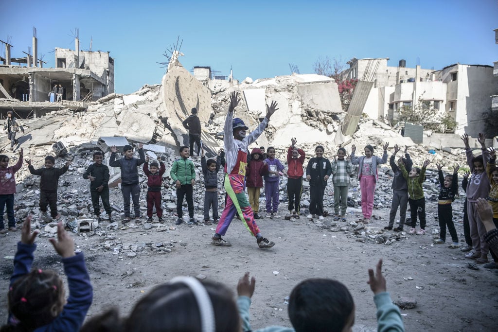 Unos niños palestinos en Rafah se manifiestan en contra de los ataques de Israel, acompañados de un payaso y los escombros que dejan los bombardeos.