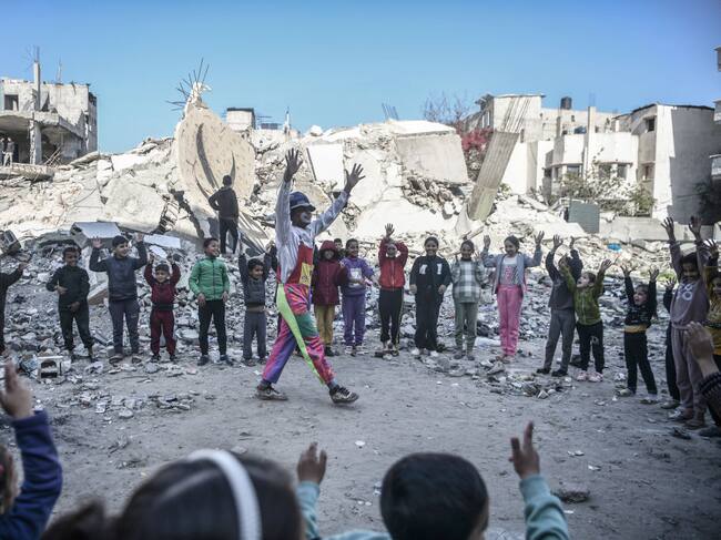 Unos niños palestinos en Rafah se manifiestan en contra de los ataques de Israel, acompañados de un payaso y los escombros que dejan los bombardeos.