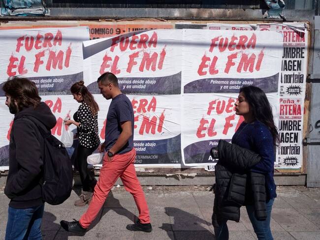 Las personas caminan ante carteles en rechazo al FMI en Buenos Aires en 2018