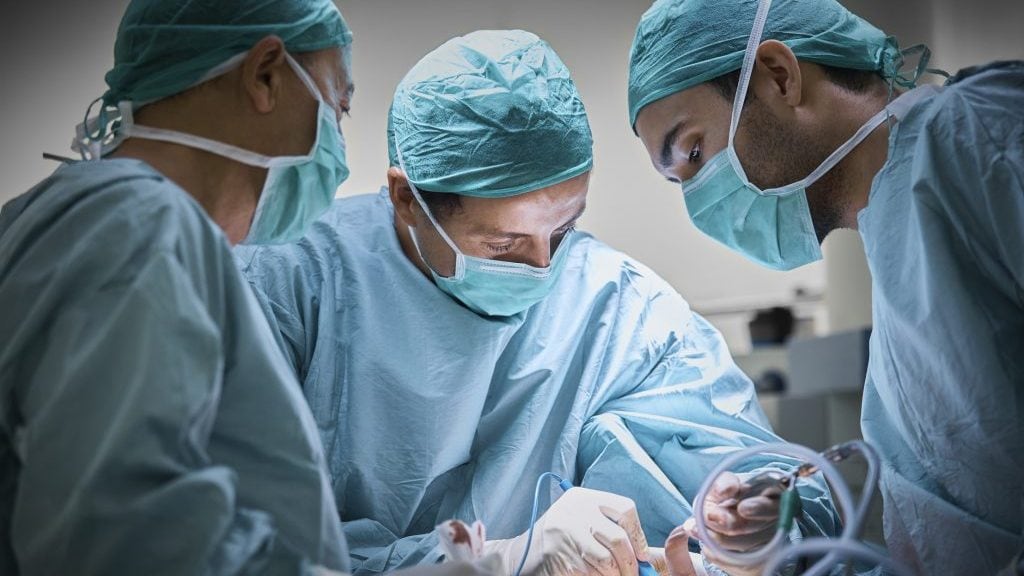Plastic surgeons operating patient for breast implant. Team of doctors are in scrubs at operating room. They are at hospital.