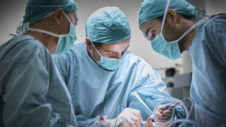 Plastic surgeons operating patient for breast implant. Team of doctors are in scrubs at operating room. They are at hospital.