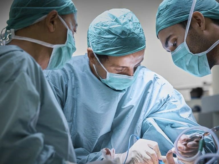 Plastic surgeons operating patient for breast implant. Team of doctors are in scrubs at operating room. They are at hospital.