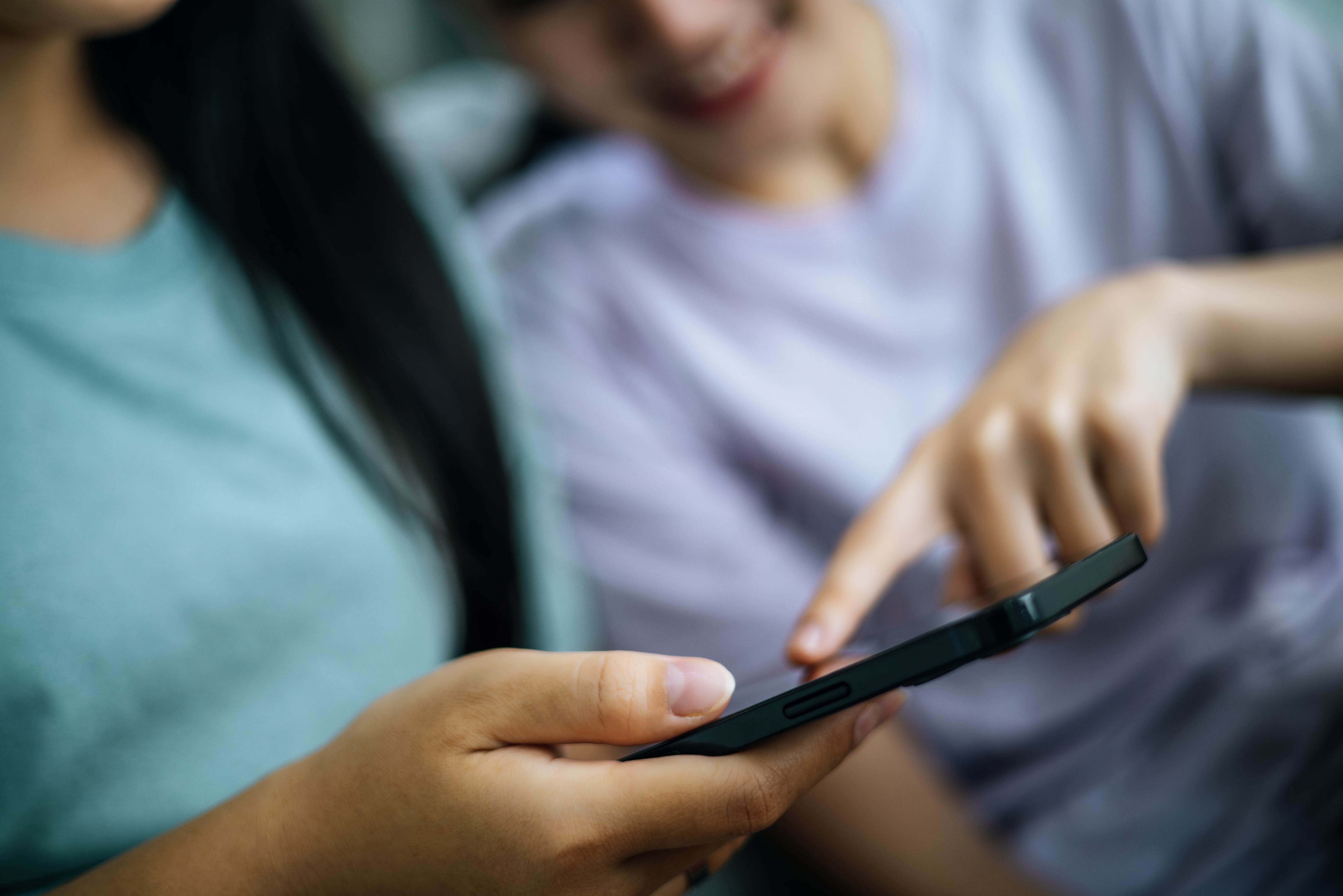 Crop image, Selective focus young woman holding smartphone in hand and her friend touch on display of mobile phone while relax in living room together