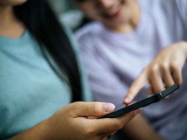 Crop image, Selective focus young woman holding smartphone in hand and her friend touch on display of mobile phone while relax in living room together