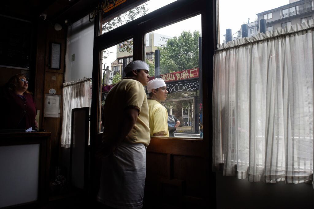 SANTIAGO, CHILE - NOVEMBER 08: Restaurant employees watch the clashes during a protest on November 8, 2019 in Santiago, Chile. Since October 18th, demonstrators demand improvements in health care, the pension system, public education, social mobility and are against the privatization of water services, the rise in public transport fares and government corruption. To contain the protests, President Sebastian Piñera had done reshuffle of cabinet and announced he would raise the minimum salary. (Photo by Claudio Santana/Getty Images)