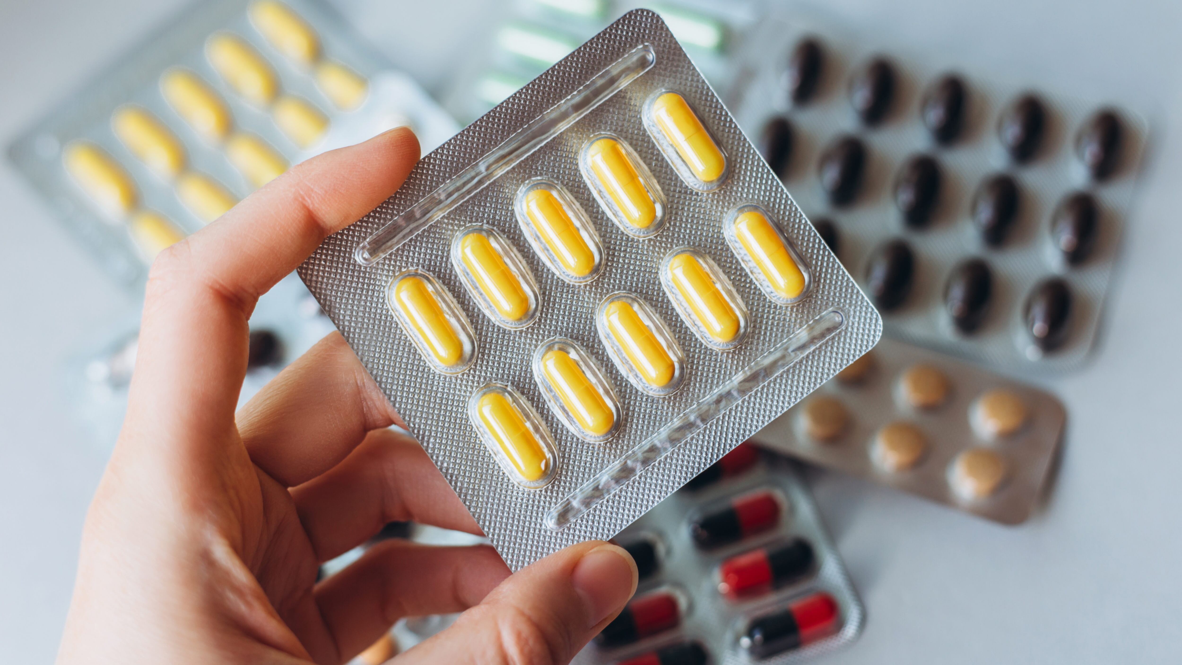 A female hand holds a package of yellow pills on the background of a heap of colored pills in packages