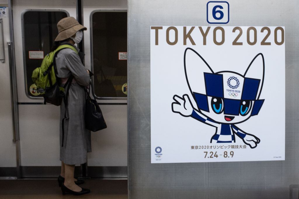 Una mujer con mascarilla junto a la publicidad de Tokio 2020