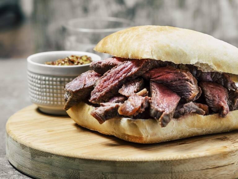 Grilled steak sandwich with a bowl of mustard on a round wooden cutting board