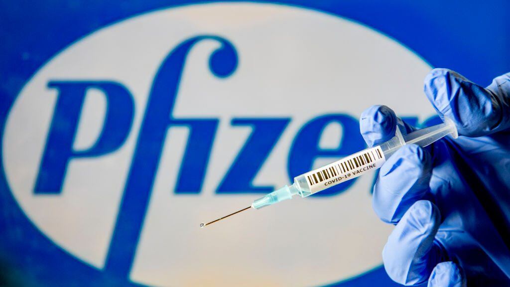 NETHERLANDS - 2020/11/29: In this photo illustration, a man holds a syringe with a fake Covid-19 vaccine with the Pfizer logo in the background. (Photo Illustration by Robin Utrecht/SOPA Images/LightRocket via Getty Images)