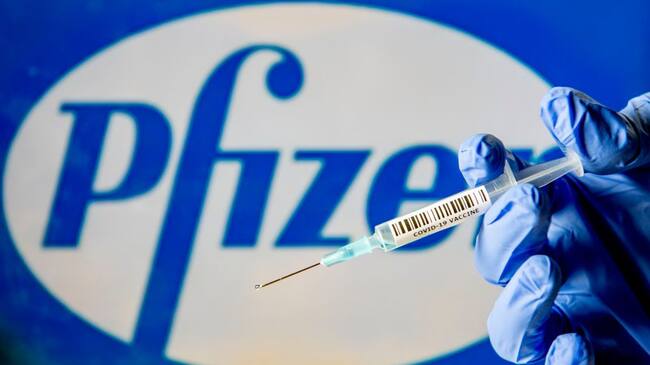 NETHERLANDS - 2020/11/29: In this photo illustration, a man holds a syringe with a fake Covid-19 vaccine with the Pfizer logo in the background. (Photo Illustration by Robin Utrecht/SOPA Images/LightRocket via Getty Images)