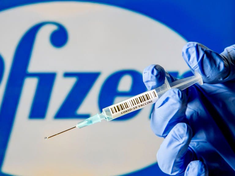 NETHERLANDS - 2020/11/29: In this photo illustration, a man holds a syringe with a fake Covid-19 vaccine with the Pfizer logo in the background. (Photo Illustration by Robin Utrecht/SOPA Images/LightRocket via Getty Images)