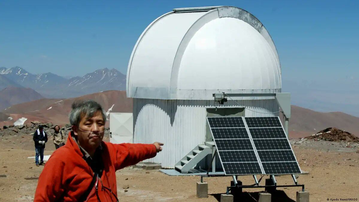 El profesor Takashi Miyata, quien lleva un dispositivo de oxígeno para enfrentar la altitud, señalando el Observatorio de Atacama (TAO) | Foto de Deutsche Welle (DW)