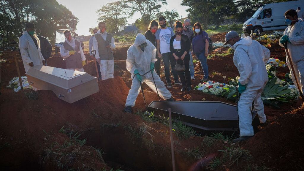 14 October 2020, Brazil, Sao Paulo: At the Vila Formosa cemetery, relatives wearing face masks watch as cemetery workers in protective suits manoeuvre a coffin during a funeral. The Ministry of Health has confirmed 955 377 Covid-19 infected and 46 510 coronavirus deaths. More than a quarter of the newly registered deaths occurred in the state of São Paulo. Photo: Lincon Zarbietti/dpa (Photo by Lincon Zarbietti/picture alliance via Getty Images)