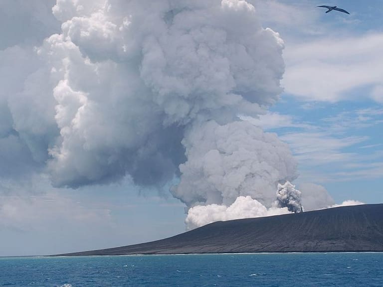 This view taken on January 17, 2015 from a boat at sea shows a frigate bird (C) flying on the thermals from the new vent as steam and gas rise from the eruption of a volcano, some 65 kilometres (40 miles) northwest of the South Pacific nation Tonga&#039;s capital Nuku&#039;alofa. The Tongan volcano has created a substantial new island since it began erupting in December, spewing out huge volumes of rock and dense ash that has killed nearby vegetation, officials said on January 16.  The Lands and Natural Resources Ministry said the volcano was erupting from two vents, one on the uninhabited island of Hunga Ha&#039;apai and the other underwater about 100 metres offshore.        AFP PHOTO / Matangi Tonga / Mary Lyn Fonua        (Photo credit should read Mary Lyn Fonua/AFP via Getty Images)