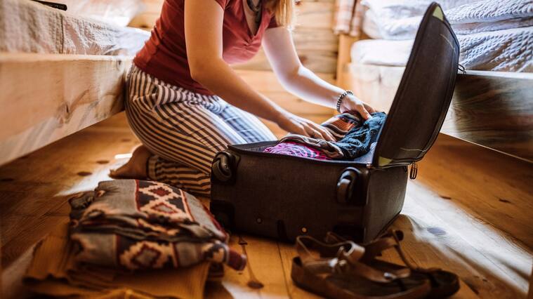Unrecognizable woman packing luggage in log cabin, sitting on floor