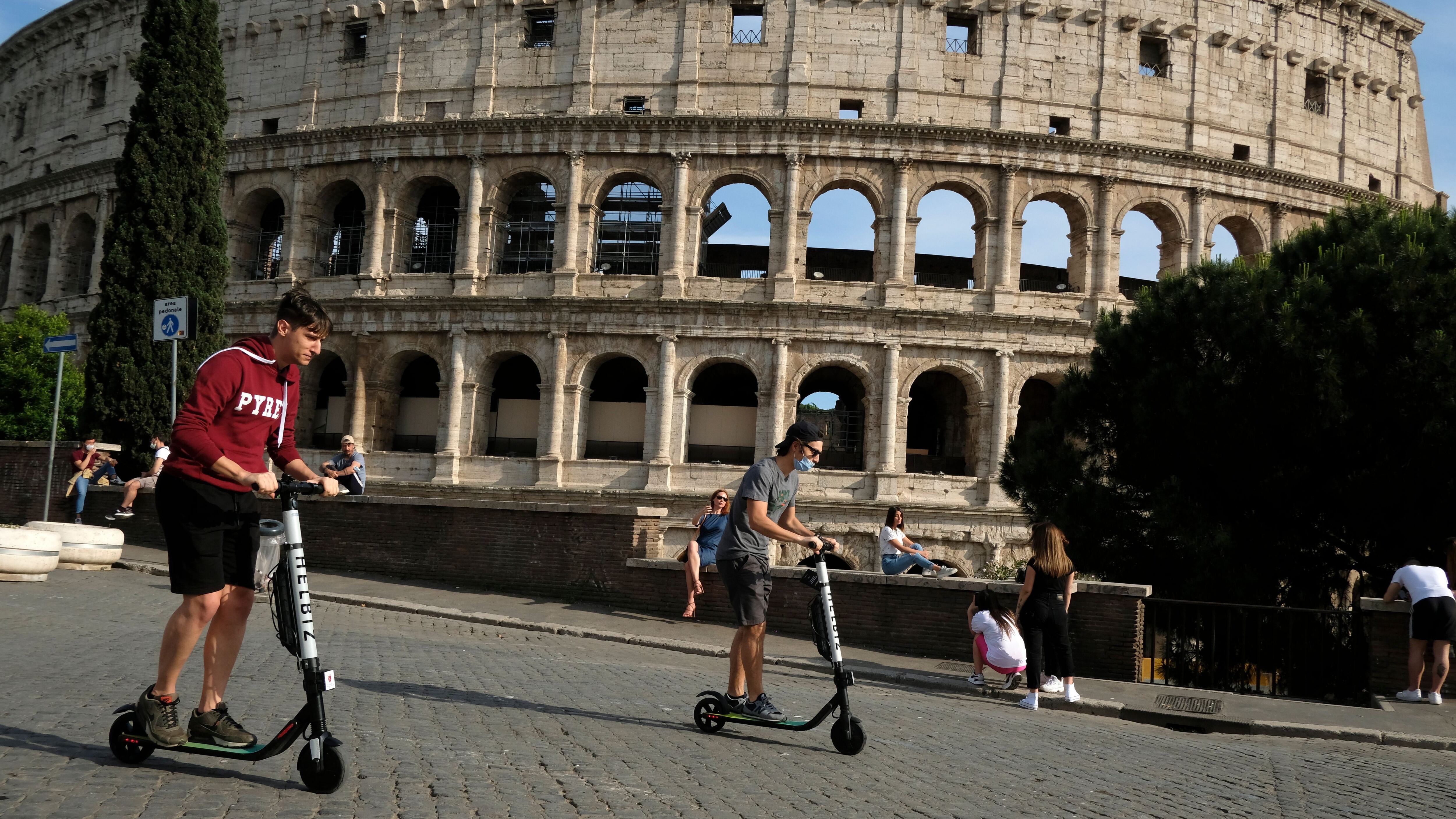 People ride electric scooters of Italian-American intra-urban transportation company Helbiz, on May 28, 2020 past the Colosseum monument in Rome as the country eases its lockdown aimed at curbing the spread of the COVID-19 infection, caused by the novel coronavirus. (Photo by Andreas SOLARO / AFP) (Photo by ANDREAS SOLARO/AFP via Getty Images)