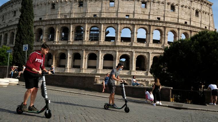 People ride electric scooters of Italian-American intra-urban transportation company Helbiz, on May 28, 2020 past the Colosseum monument in Rome as the country eases its lockdown aimed at curbing the spread of the COVID-19 infection, caused by the novel coronavirus. (Photo by Andreas SOLARO / AFP) (Photo by ANDREAS SOLARO/AFP via Getty Images)