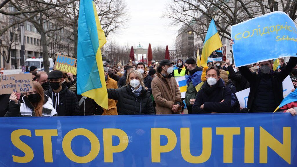 BERLIN, GERMANY - FEBRUARY 22:  A woman holds a Ukrainian flag next to a banner reading stop Putin as youth groups protest Ukraine intervention with human chain in front of the Russian Embassy on February 22, 2022 in Berlin, Germany. Yesterday, Russia recognized two breakaway regions of eastern Ukraine as independent republics and said it would send troops in "peacekeeping functions," prompting widespread condemnation from Western governments. (Photo by Omer Messinger/Getty Images)