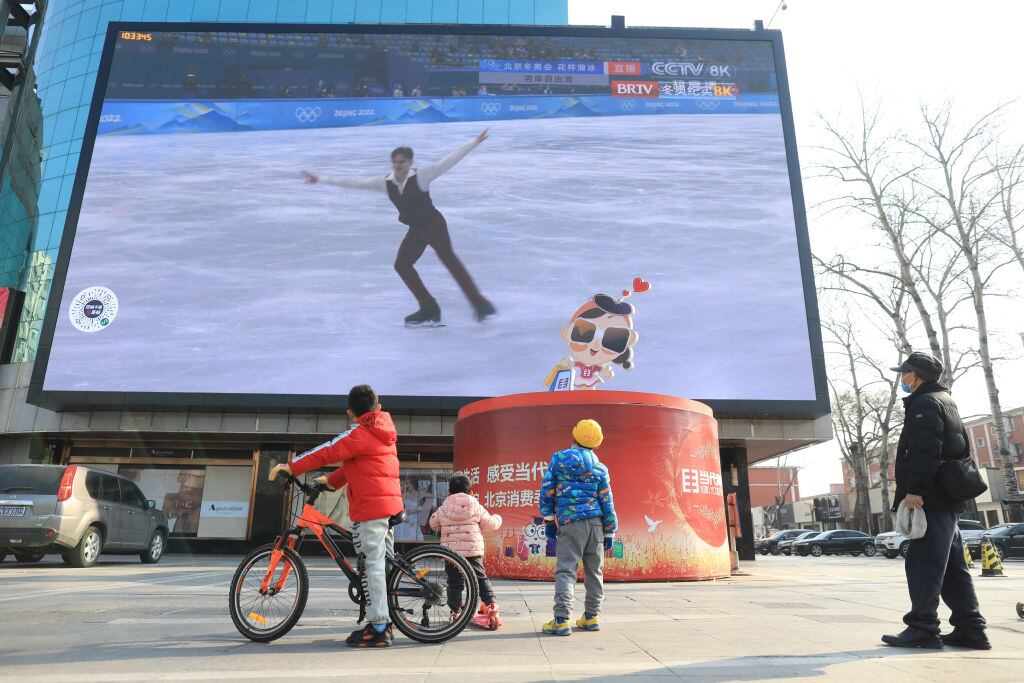 Personas observan los juegos de Pekín 2022 en un televisor en la calle