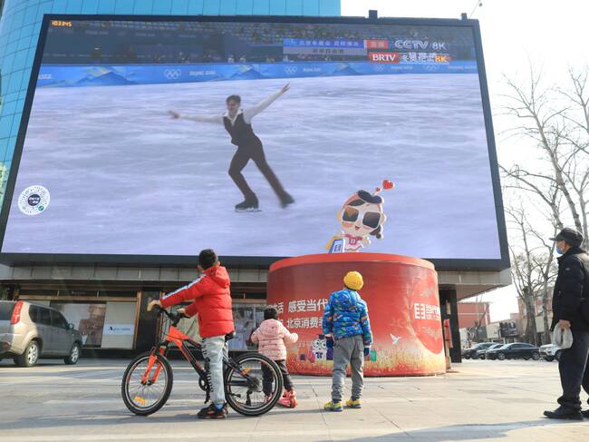 Personas observan los juegos de Pekín 2022 en un televisor en la calle