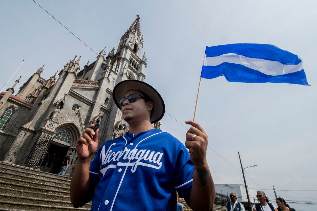 Un hombre con la bandera de Nicaragua camina en una procesión frente a un iglesia católica.