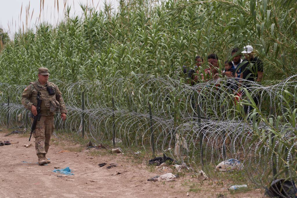 Un militar de Estados Unidos vigila la frontera ante unos inmigrantes