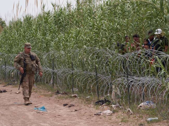 Un militar de Estados Unidos vigila la frontera ante unos inmigrantes