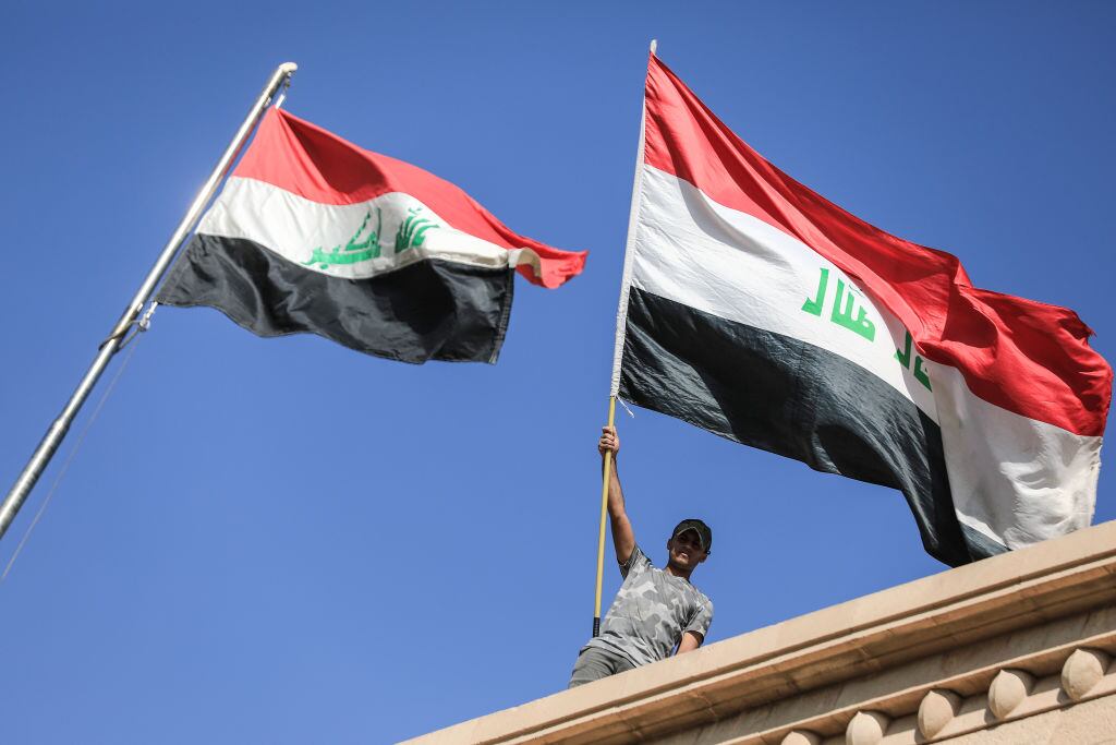Manifestantes con la bandera de Irak en el techo del palacio de gobierno