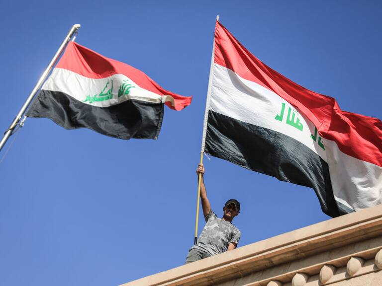 Manifestantes con la bandera de Irak en el techo del palacio de gobierno