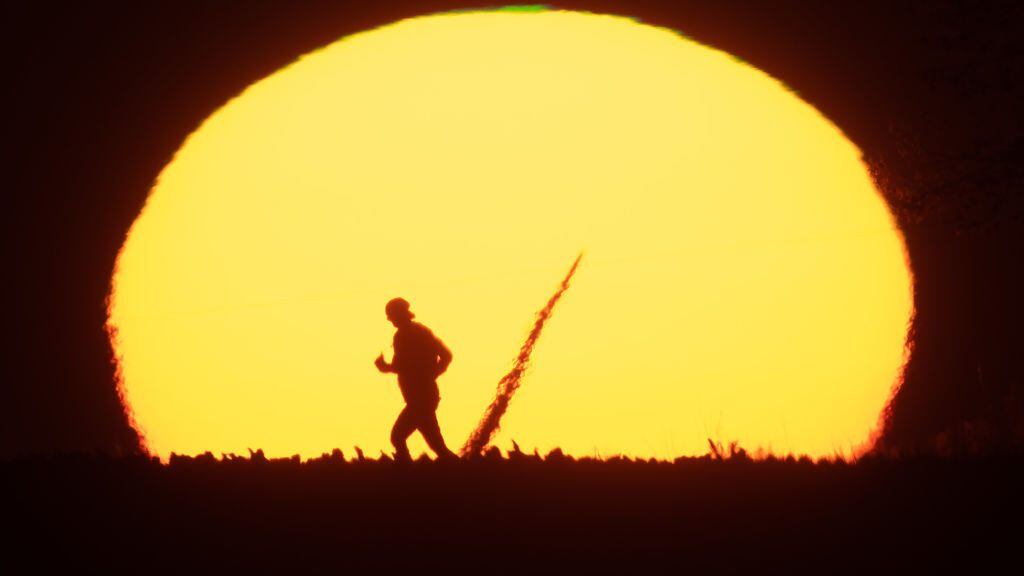 21 September 2020, Lower Saxony, Algermissen: A woman is jogging in the early morning at sunrise over a field path in the district of Hildesheim. A rotor blade of a wind turbine can also be seen in the sun. Photo: Julian Stratenschulte/dpa (Photo by Julian Stratenschulte/picture alliance via Getty Images)