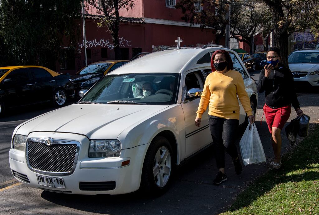 People walk past a funeral home car parked outside the San Jose public hospital morgue, amid the spread of the coronavirus disease (COVID-19) in Santiago, on June 05, 2020. - Deaths from the coronavirus in Chile have risen by more than 50 percent in the past week, the health ministry announced Friday, despite a three-week lockdown of the capital Santiago. Three months after the country registered its first infection, Health Minister Jaime Manalich reported 4,207 new infections and 92 deaths in the previous 24 hours. (Photo by MARTIN BERNETTI / AFP) (Photo by MARTIN BERNETTI/AFP via Getty Images)