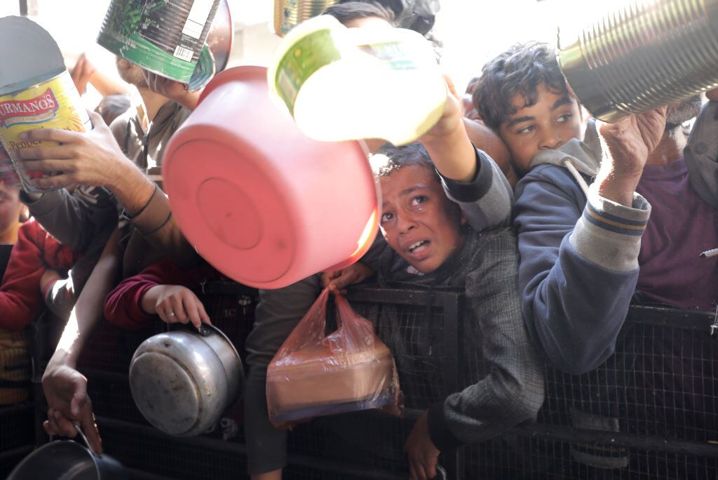 Niños, mujeres y hombres buscan alimentos para colocar en sus inventados plato de comida en la Franja de Gaza en Palestina