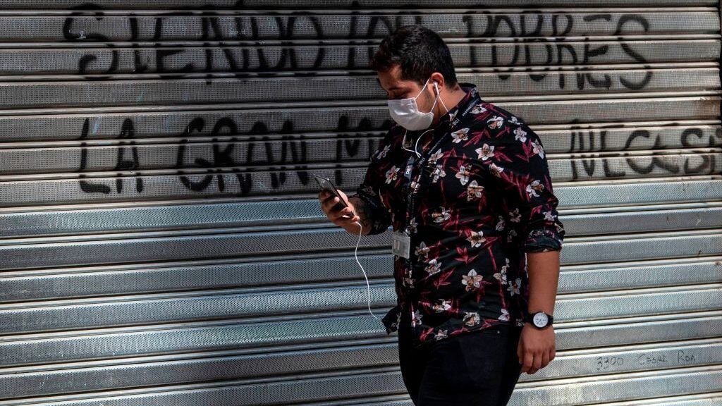 A man wears a face mask as he uses his mobile phone while walking in a street of Santiago, on April 06, 2020, amid the neew coronavirus pandemic. (Photo by MARTIN BERNETTI / AFP) (Photo by MARTIN BERNETTI/AFP via Getty Images)