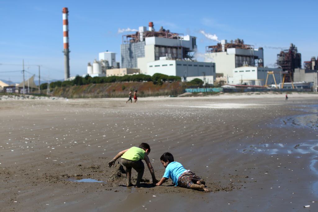 TOPSHOT - Children play in the sand at Las Ventanas beach next to the AES Gener thermoelectric plant in Puchuncavi, Valparaiso region, Chile, on October 8, 2019. - The Quintero-Puchuncavi has become one of the five "sacrifice zones" in Chile since an industrial cord has polluted air, land and sea for decades. Some 50,000 victims breathe daily the gases aired by some 15 industries including four coal-fired thermoelectric power plants, crude and copper refineries. (Photo by Pablo VERA / AFP) (Photo by PABLO VERA/AFP via Getty Images)