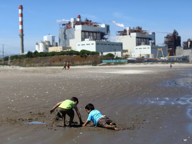 TOPSHOT - Children play in the sand at Las Ventanas beach next to the AES Gener thermoelectric plant in Puchuncavi, Valparaiso region, Chile, on October 8, 2019. - The Quintero-Puchuncavi has become one of the five "sacrifice zones" in Chile since an industrial cord has polluted air, land and sea for decades. Some 50,000 victims breathe daily the gases aired by some 15 industries including four coal-fired thermoelectric power plants, crude and copper refineries. (Photo by Pablo VERA / AFP) (Photo by PABLO VERA/AFP via Getty Images)