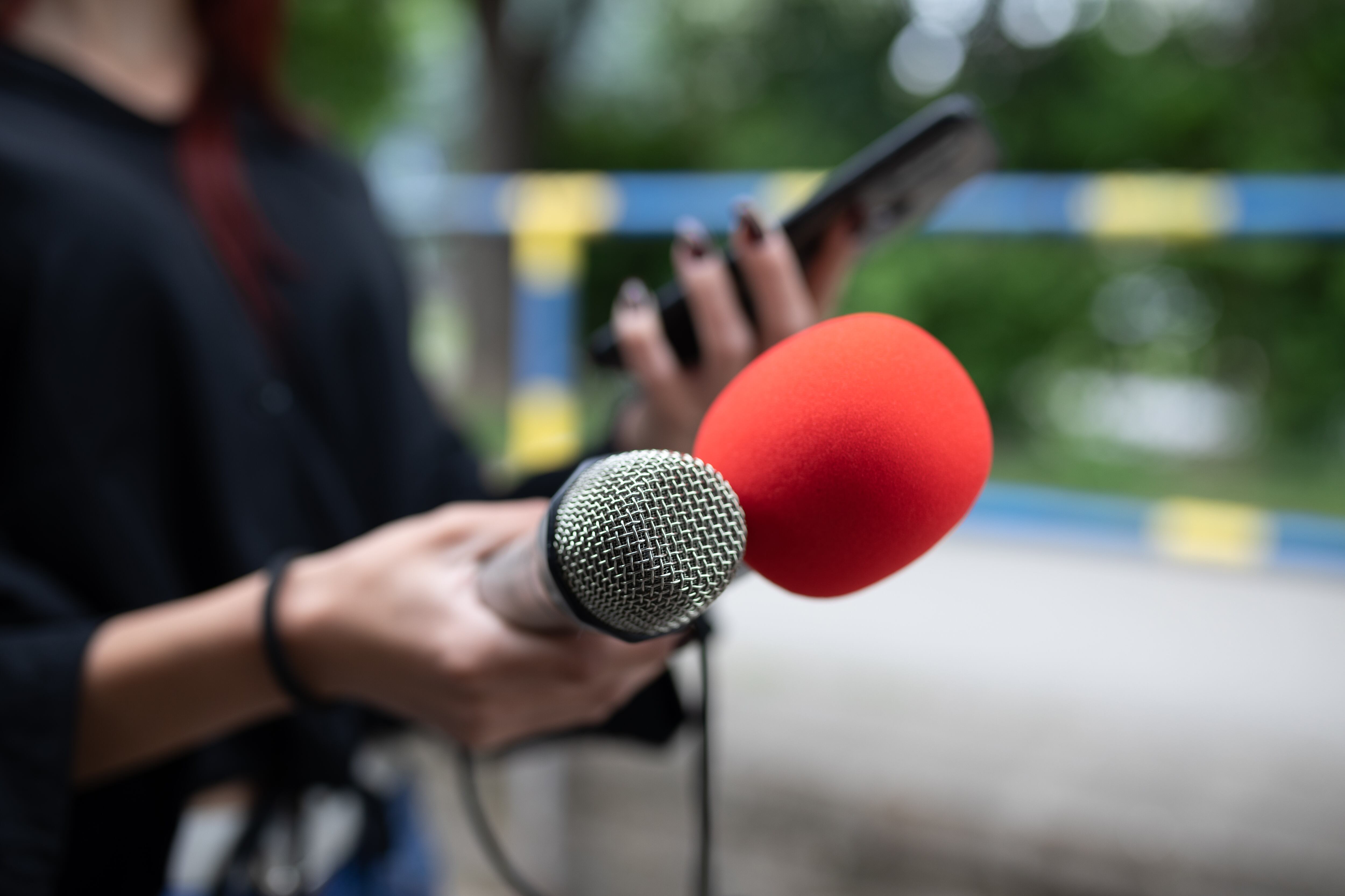 Female journalist at news conference, recording notes, holding microphone and smarthopne lice dictaphone