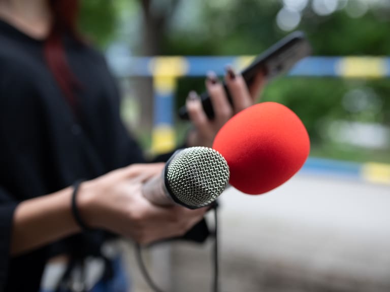 Female journalist at news conference, recording notes, holding microphone and smarthopne lice dictaphone