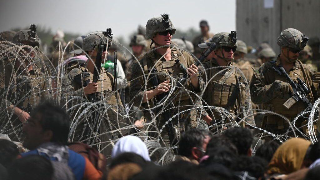 US soldiers stand guard behind barbed wire as Afghans sit on a roadside near the military part of the airport in Kabul on August 20, 2021, hoping to flee from the country after the Taliban's military takeover of Afghanistan. (Photo by Wakil KOHSAR / AFP) (Photo by WAKIL KOHSAR/AFP via Getty Images)