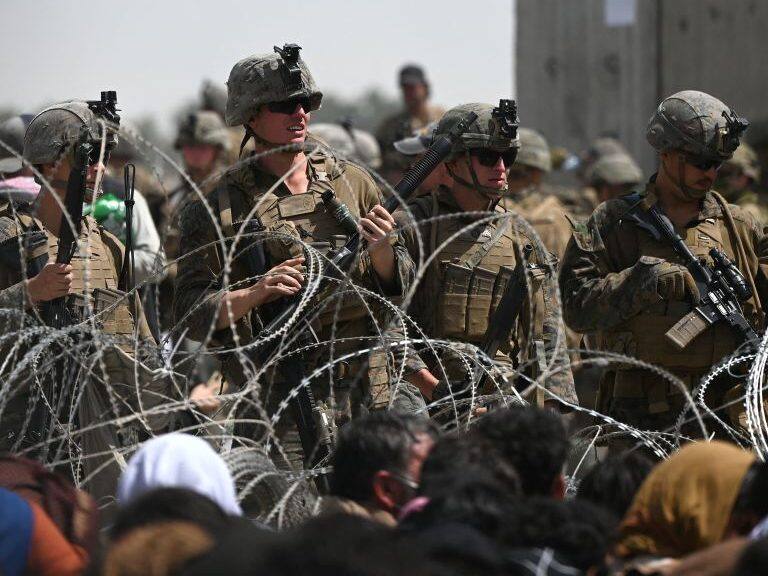 US soldiers stand guard behind barbed wire as Afghans sit on a roadside near the military part of the airport in Kabul on August 20, 2021, hoping to flee from the country after the Taliban's military takeover of Afghanistan. (Photo by Wakil KOHSAR / AFP) (Photo by WAKIL KOHSAR/AFP via Getty Images)