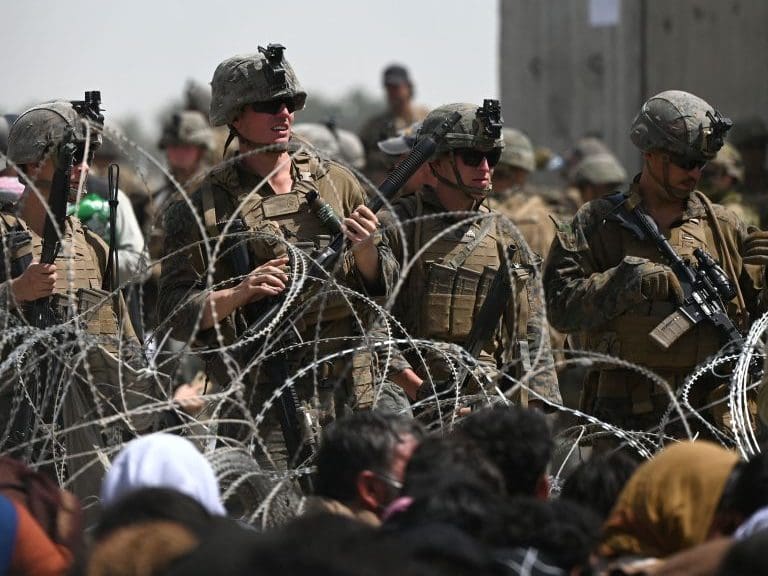 US soldiers stand guard behind barbed wire as Afghans sit on a roadside near the military part of the airport in Kabul on August 20, 2021, hoping to flee from the country after the Taliban&#039;s military takeover of Afghanistan. (Photo by Wakil KOHSAR / AFP) (Photo by WAKIL KOHSAR/AFP via Getty Images)