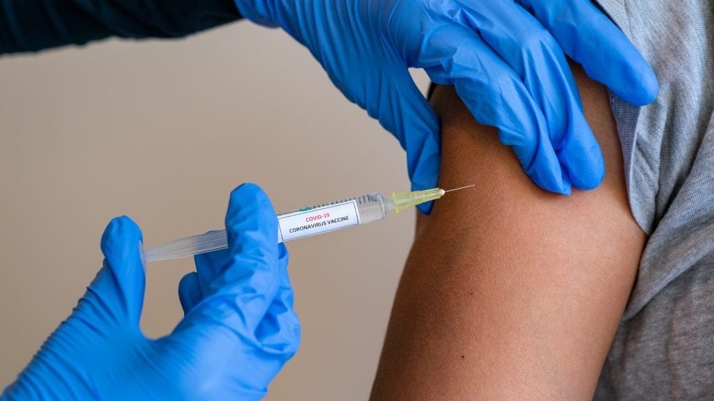 This picture depicts a young female clinician using a syringe to inject a concept COVD-19 liquid vaccine into a young girl patient during the Phase 3 vaccination human trials.