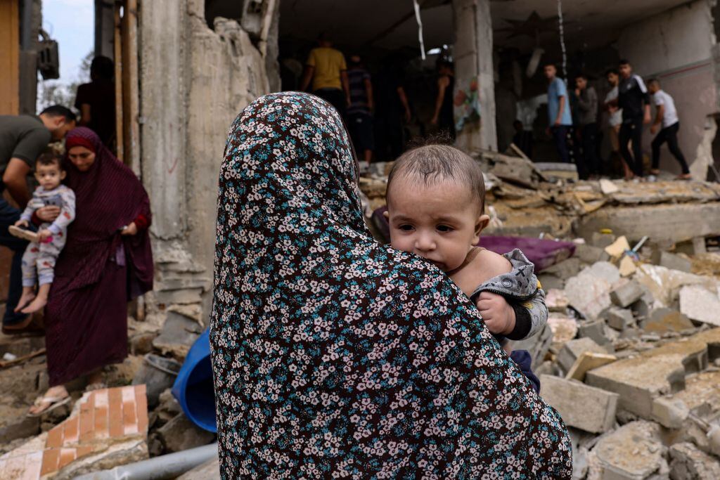 Un bebé llevado por una mujer en medio de la destrucción en Gaza