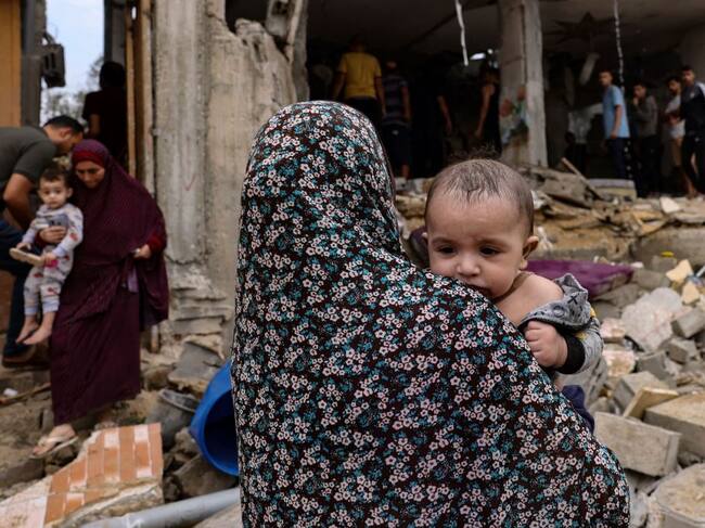 Un bebé llevado por una mujer en medio de la destrucción en Gaza
