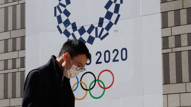 TOKYO, JAPAN - 2021/03/04: A pedestrian wearing a mask walks by a signage advertising the Tokyo 2020 Olympic Games in Tokyo. International Olympic Committee (IOC) President Thomas Bach reiterated that the IOC is fully committed to delivering the Tokyo Games this summer. The opening ceremony is currently scheduled for July 23. (Photo by James Matsumoto/SOPA Images/LightRocket via Getty Images)