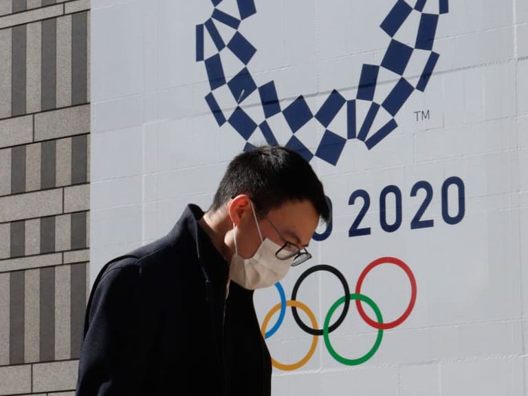 TOKYO, JAPAN - 2021/03/04: A pedestrian wearing a mask walks by a signage advertising the Tokyo 2020 Olympic Games in Tokyo. International Olympic Committee (IOC) President Thomas Bach reiterated that the IOC is fully committed to delivering the Tokyo Games this summer. The opening ceremony is currently scheduled for July 23. (Photo by James Matsumoto/SOPA Images/LightRocket via Getty Images)