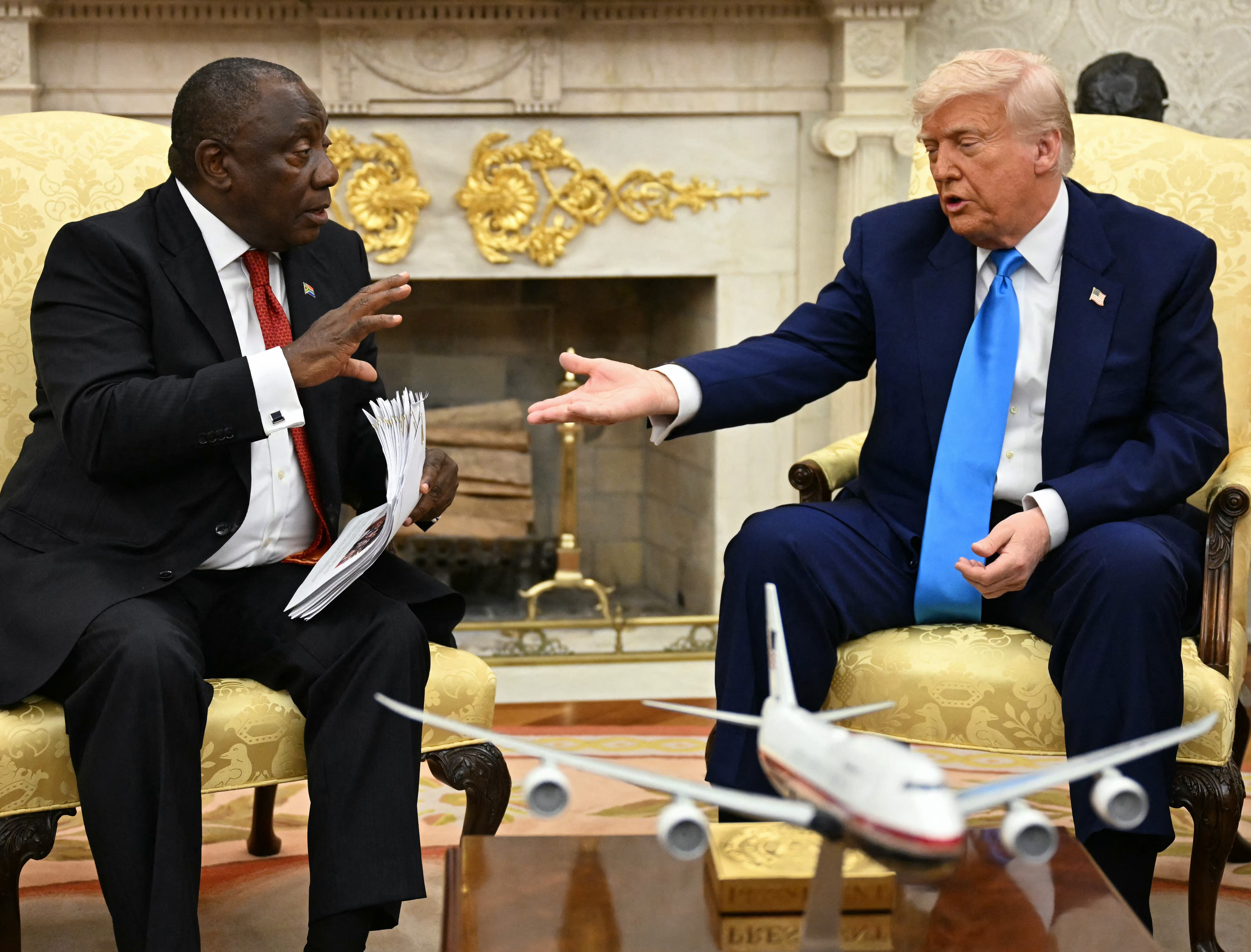 TOPSHOT - US President Donald Trump hands papers to South African President Cyril Ramaphosa during a meeting in the Oval Office of the White House in Washington, DC, on May 21, 2025. South African President Cyril Ramaphosa meets Donald Trump on Wednesday amid tensions over Washington's resettlement of white Afrikaners that the US president claims are the victims of "genocide." (Photo by Jim WATSON / AFP) (Photo by JIM WATSON/AFP via Getty Images)