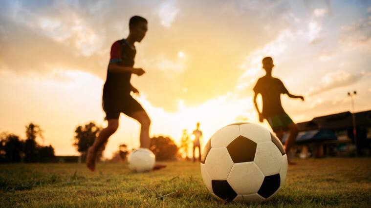action sport outdoors of a group of kids having fun playing soccer football on the dirt field.