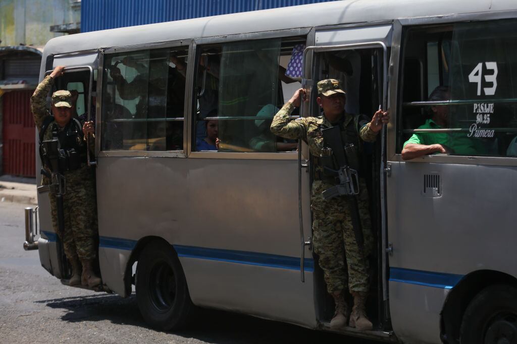 Soldados de El Salvador vigilan las calles y a las personas a bordo de un bus del transporte público en la ciudad de San Salvador.